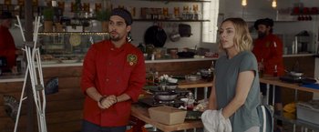 Movie still from “That's Amor” (2022), directed by Shaun Paul Piccinino – A man and a woman standing in front of a counter; Medium shot, Over the shoulder angle