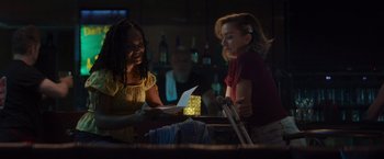 Movie still from “That's Amor” (2022), directed by Shaun Paul Piccinino – Two women sitting at a table in a dark room; Medium shot, Over the shoulder angle