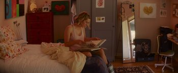 Movie still from “That's Amor” (2022), directed by Shaun Paul Piccinino – A woman sitting on top of a bed reading a magazine; Medium shot, Low angle