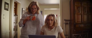 Movie still from “That's Amor” (2022), directed by Shaun Paul Piccinino – A woman and a woman standing next to a laptop; Medium shot, Over the shoulder angle