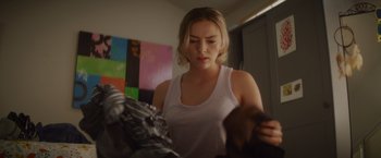 Movie still from “That's Amor” (2022), directed by Shaun Paul Piccinino – A woman in a white tank top is looking at a pair of shoes; Medium shot, Over the shoulder angle