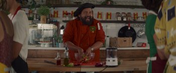 Movie still from “That's Amor” (2022), directed by Shaun Paul Piccinino – A man with a beard is cutting vegetables; Medium shot, Over the shoulder angle