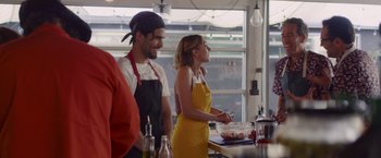 Movie still from “That's Amor” (2022), directed by Shaun Paul Piccinino – A man and a woman standing next to each other in front of a counter; Medium shot, Over the shoulder angle