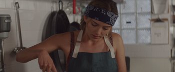 Movie still from “That's Amor” (2022), directed by Shaun Paul Piccinino – A woman wearing an apron and a bandanna; Close Up shot, Low angle