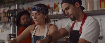 Movie still from “That's Amor” (2022), directed by Shaun Paul Piccinino – A man and a woman working together in a kitchen; Medium shot, Low angle