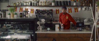 Movie still from “That's Amor” (2022), directed by Shaun Paul Piccinino – A man standing behind a counter in a restaurant; Wide shot, Low angle
