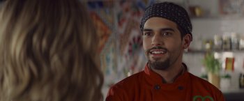 Movie still from “That's Amor” (2022), directed by Shaun Paul Piccinino – A man in a red shirt and a woman in a black hat; Close Up shot, Over the shoulder angle