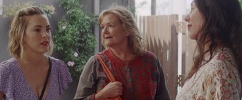 Movie still from “That's Amor” (2022), directed by Shaun Paul Piccinino – A woman holding an orange purse while standing outside; Close Up shot, Over the shoulder angle