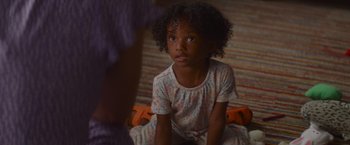 Movie still from “That's Amor” (2022), directed by Shaun Paul Piccinino – A little girl sitting on the floor in her pajamas; Close Up shot, High angle