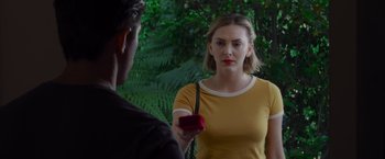 Movie still from “That's Amor” (2022), directed by Shaun Paul Piccinino – A woman holding a red box in front of a man; Medium shot, Over the shoulder angle