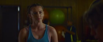 Movie still from “That's Amor” (2022), directed by Shaun Paul Piccinino – A woman is standing in a gym with a ball in the background; Close Up shot, Over the shoulder angle