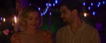 Movie still from “That's Amor” (2022), directed by Shaun Paul Piccinino – A man and a woman standing next to each other in front of lights; Close Up shot, Over the shoulder angle
