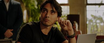 Movie still from “The 355” (2022), directed by Simon Kinberg – A person sitting down with his hand up to his ear; Close Up shot, Over the shoulder angle