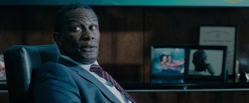 Movie still from “The 355” (2022), directed by Simon Kinberg – A man in a suit sitting in front of a tv; Close Up shot, Over the shoulder angle