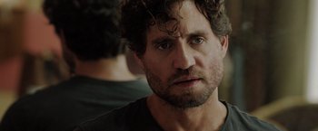 Movie still from “The 355” (2022), directed by Simon Kinberg – A person with curly hair and a beard; Close Up shot, Over the shoulder angle