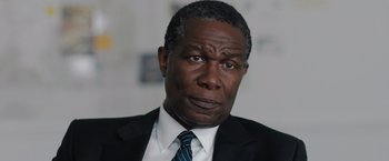 Movie still from “The 355” (2022), directed by Simon Kinberg – An older man in a suit and tie looking at the camera; Close Up shot, Over the shoulder angle