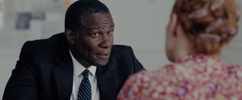 Movie still from “The 355” (2022), directed by Simon Kinberg – A man in a suit and tie talking to a woman in a floral dress; Close Up shot, Over the shoulder angle