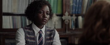Movie still from “The 355” (2022), directed by Simon Kinberg – A woman in a vest and tie sitting in front of a bookshelf; Close Up shot, Over the shoulder angle