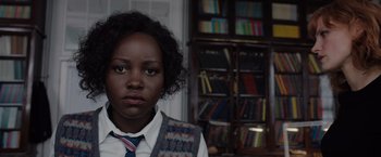 Movie still from “The 355” (2022), directed by Simon Kinberg – A woman in a tie standing in front of bookshelves; Close Up shot, Over the shoulder angle