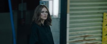 Movie still from “The 355” (2022), directed by Simon Kinberg – A woman in a black hoodie standing in front of a building; Close Up shot, Over the shoulder angle