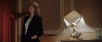 Movie still from “The 355” (2022), directed by Simon Kinberg – A woman standing in front of a lamp in a darkened room; Medium shot, Low angle