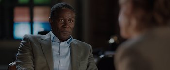 Movie still from “The 355” (2022), directed by Simon Kinberg – An older man in a gray suit and blue shirt; Close Up shot, Over the shoulder angle