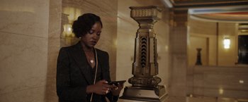 Movie still from “The 355” (2022), directed by Simon Kinberg – A woman standing in front of a statue looking at her cell phone; Medium shot, Low angle