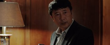 Movie still from “The 355” (2022), directed by Simon Kinberg – An older man wearing a suit and a white shirt; Close Up shot, Low angle