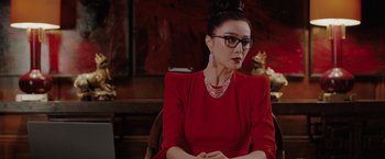 Movie still from “The 355” (2022), directed by Simon Kinberg – A woman in a red dress sitting in front of a table; Medium shot, Over the shoulder angle