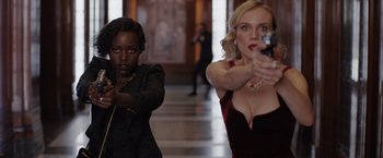 Movie still from “The 355” (2022), directed by Simon Kinberg – Two women in formal attire holding guns in a hallway; Medium shot, Over the shoulder angle
