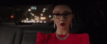 Movie still from “The 355” (2022), directed by Simon Kinberg – A woman wearing glasses and a red dress in the back of a car; Close Up shot, Over the shoulder angle