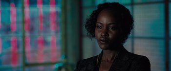 Movie still from “The 355” (2022), directed by Simon Kinberg – A black woman with curly black hair wearing a black jacket; Close Up shot, Over the shoulder angle
