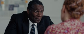 Movie still from “The 355” (2022), directed by Simon Kinberg – A man in a suit and tie looking at the camera; Close Up shot, Over the shoulder angle