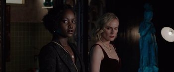 Movie still from “The 355” (2022), directed by Simon Kinberg – Two beautiful women standing next to each other in a dark room; Close Up shot, Over the shoulder angle
