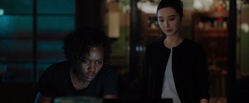 Movie still from “The 355” (2022), directed by Simon Kinberg – Two people are sitting in a dark room looking at a laptop; Close Up shot, Over the shoulder angle