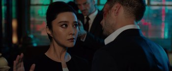 Movie still from “The 355” (2022), directed by Simon Kinberg – A woman and a man in a suit and tie in front of other men; Close Up shot, Over the shoulder angle