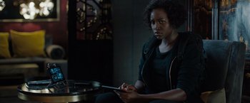 Movie still from “The 355” (2022), directed by Simon Kinberg – A woman sitting in a dark room holding a tablet computer; Medium shot, Over the shoulder angle