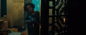 Movie still from “The 355” (2022), directed by Simon Kinberg – A woman holding a gun while standing next to a wall; Medium shot, Over the shoulder angle