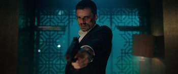 Movie still from “The 355” (2022), directed by Simon Kinberg – A man in a black suit holding a gun in his hand; Close Up shot, Low angle
