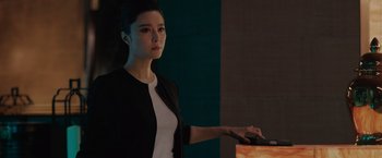 Movie still from “The 355” (2022), directed by Simon Kinberg – A young woman in a black jacket is playing a video game; Medium shot, Over the shoulder angle