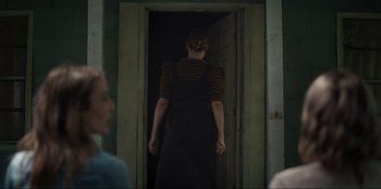 Movie still from “The Accursed” (2022), directed by Kevin Lewis – A woman in a striped shirt is walking through an open door; Medium shot, Over the shoulder angle
