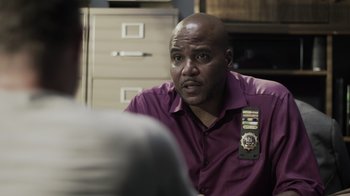Movie still from “The Amityville Moon” (2021), directed by Thomas J. Churchill – A man in purple shirt sitting in front of another man; Close Up shot, Over the shoulder angle