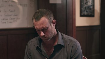 Movie still from “The Amityville Moon” (2021), directed by Thomas J. Churchill – A person wearing a gray shirt; Close Up shot, Low angle