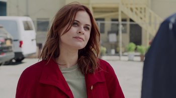 Movie still from “The Amityville Moon” (2021), directed by Thomas J. Churchill – A woman in a red jacket is standing in front of a building; Close Up shot, Low angle