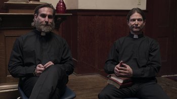 Movie still from “The Amityville Moon” (2021), directed by Thomas J. Churchill – A couple of men sitting next to each other; Medium shot, High angle