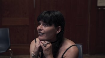 Movie still from “The Amityville Moon” (2021), directed by Thomas J. Churchill – A woman sitting in front of a wooden wall with her hand on her chin; Close Up shot, High angle