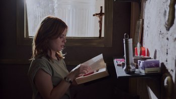 Movie still from “The Amityville Moon” (2021), directed by Thomas J. Churchill – A woman sitting at a table reading a book; Medium shot, Low angle