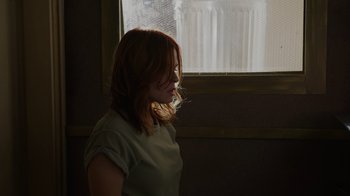 Movie still from “The Amityville Moon” (2021), directed by Thomas J. Churchill – A woman standing in front of a window with her head turned to the side; Medium shot, Over the shoulder angle