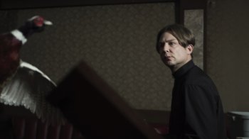 Movie still from “The Amityville Moon” (2021), directed by Thomas J. Churchill – A man standing in front of a wooden box; Medium shot, Low angle