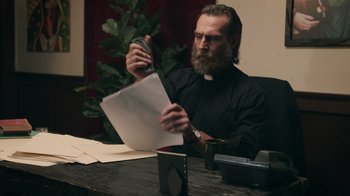 Movie still from “The Amityville Moon” (2021), directed by Thomas J. Churchill – A man sitting at a table with papers in front of him; Medium shot, Over the shoulder angle